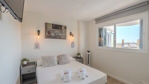 Una habitación de hotel con cama, ventana con vistas, una obra de arte en la pared y una lámpara fijada a la pared.
