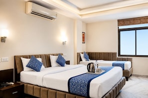 A hotel room with two beds, an air conditioning unit, bedside lamps, a window with a view, and a framed picture on the wall. - Hotel Sahibs Corporate Inn Jaipur (Jaipur)