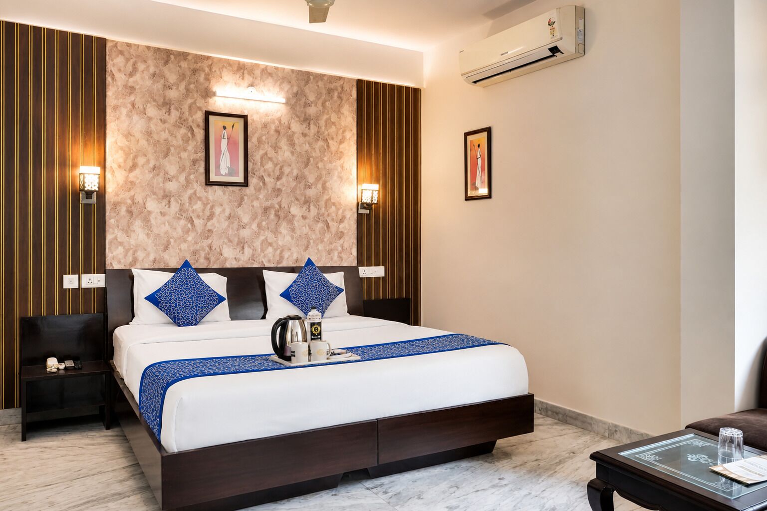 Une chambre d’hôtel avec un grand lit, deux tables de chevet, une commode, une table basse et un appareil de climatisation.