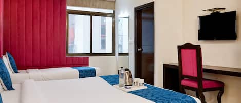 A hotel room with two beds, a desk, a chair, a TV, and a window with a view of buildings.