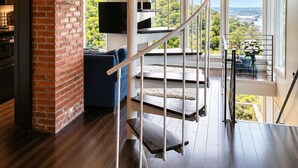 A modern interior with a spiral staircase, a brick fireplace, and large windows offering a view of greenery.