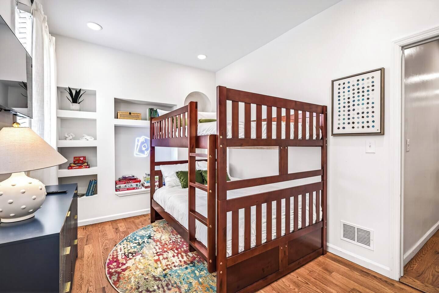A bedroom with a bunk bed, a desk with a lamp, a bookshelf, and a patterned rug.