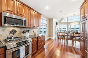 A kitchen with wooden cabinets, stainless steel appliances, a tiled backsplash, and a dining area with a chandelier.