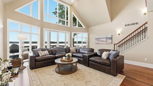 A spacious living room with a sectional sofa, a coffee table, and large windows offering a view of the outdoors. - Lakeview on Magician- lakefront luxury (Dowagiac)