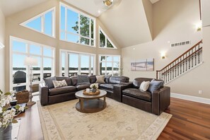 A spacious living room with a sectional sofa, a coffee table, and large windows offering a view of the outdoors.