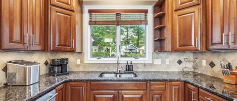 A kitchen with wooden cabinets, a granite countertop, a stainless steel sink, and a window with blinds.