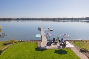 A lakeside patio with outdoor seating and a dock extending into the water. - Lakeview on Magician- lakefront luxury (Dowagiac)