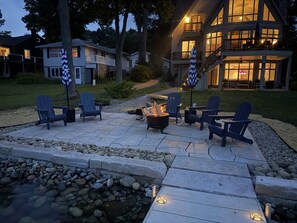 A patio with Adirondack chairs, a fire pit, and a stone pathway leading to a house. - Lakeview on Magician- lakefront luxury (Dowagiac)