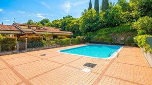 Une piscine dont le fond est recouvert de carrelage, entourée de verdure et bordée d’un bâtiment dont le toit est également recouvert de tuiles.