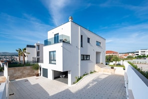 A modern white building with a flat roof, large windows, and a visible car parked in a covered area. - Villa Olivetum (Okrug Gornji)