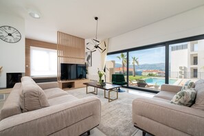 Ein modernes Wohnzimmer mit Fernseher, Sofa und großem Fenster mit Blick auf einen Pool und Gebäude.
