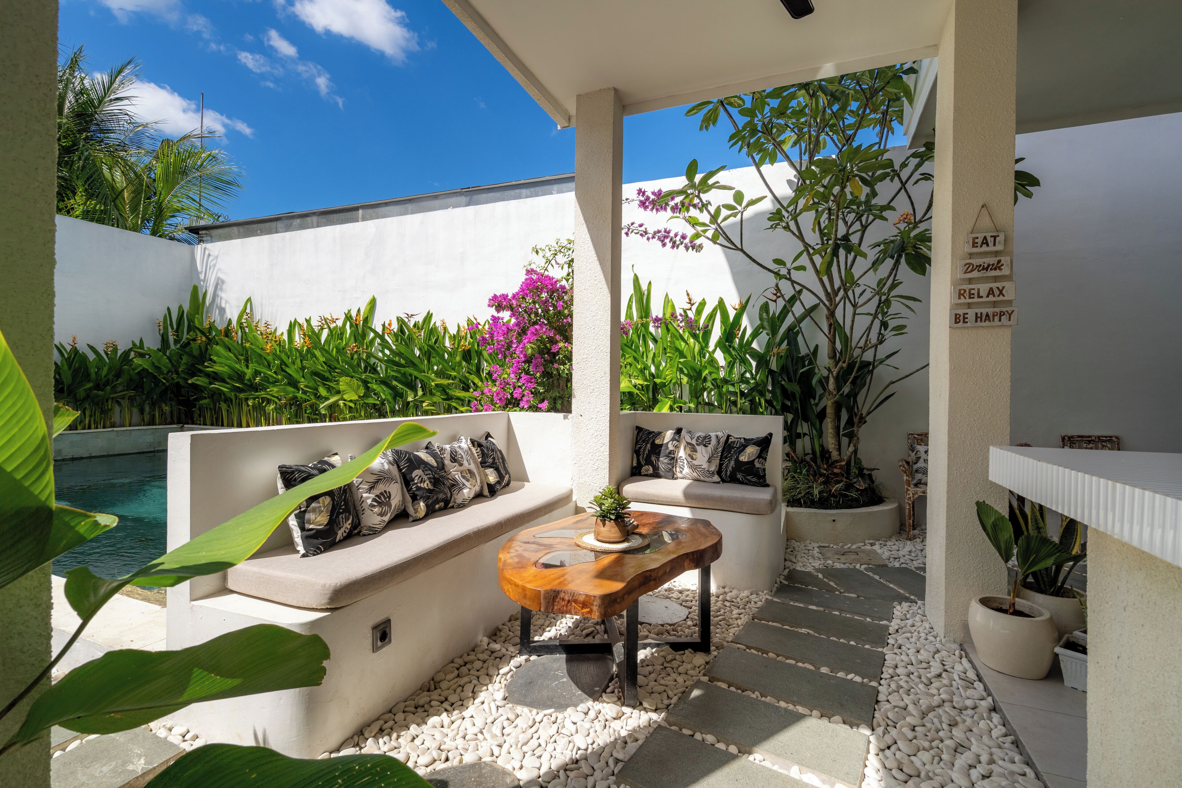 A modern outdoor seating area with a pool, white walls, and tropical plants.