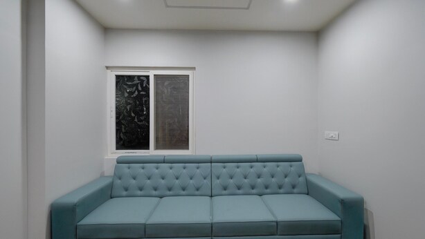 A light blue sofa in a room with white walls and a window. - Deluxe Room Adithya Stay (Hyderabad)