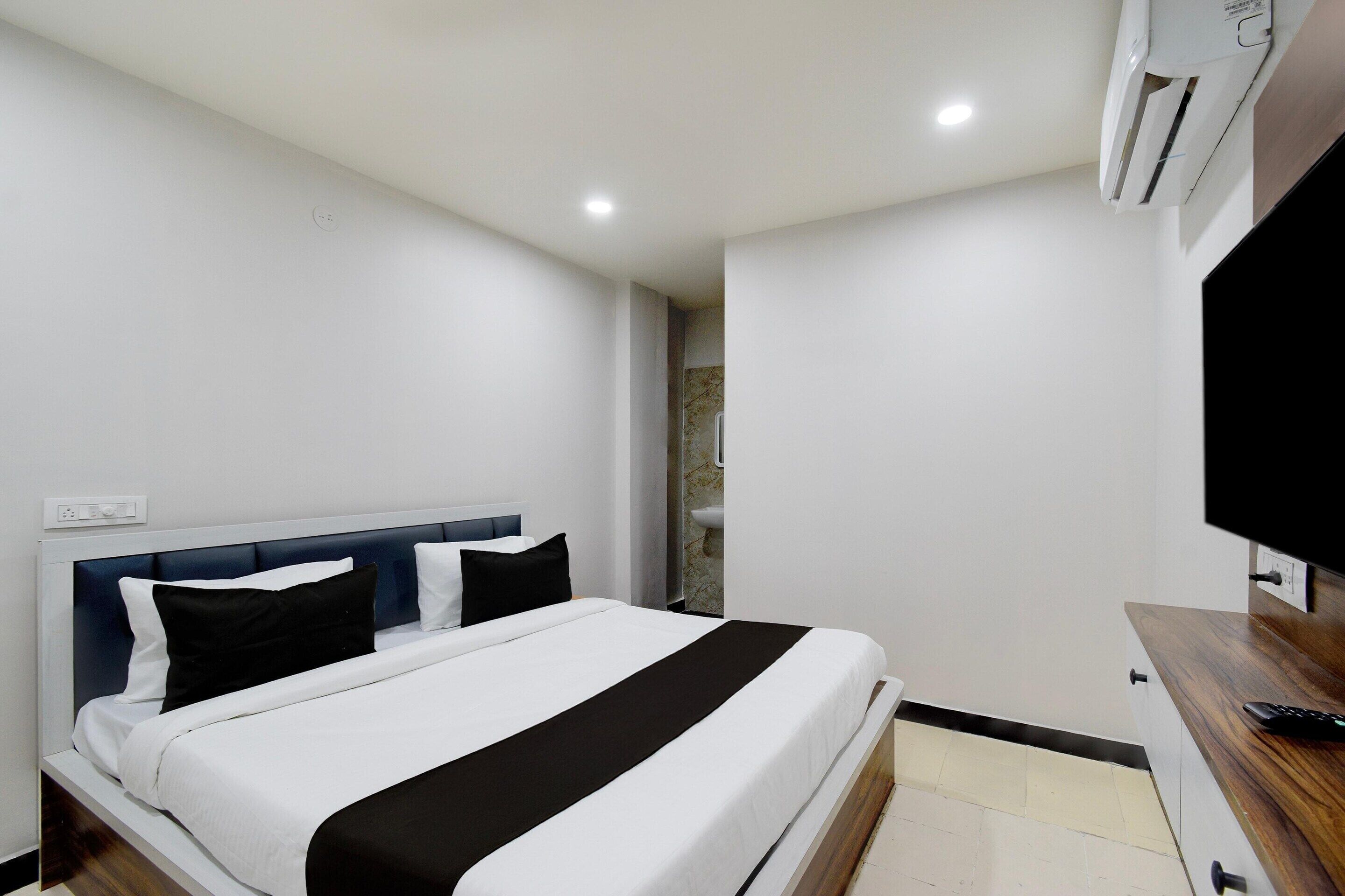 A hotel room with a bed, a TV, an air conditioner, and a bathroom with a marble wall.