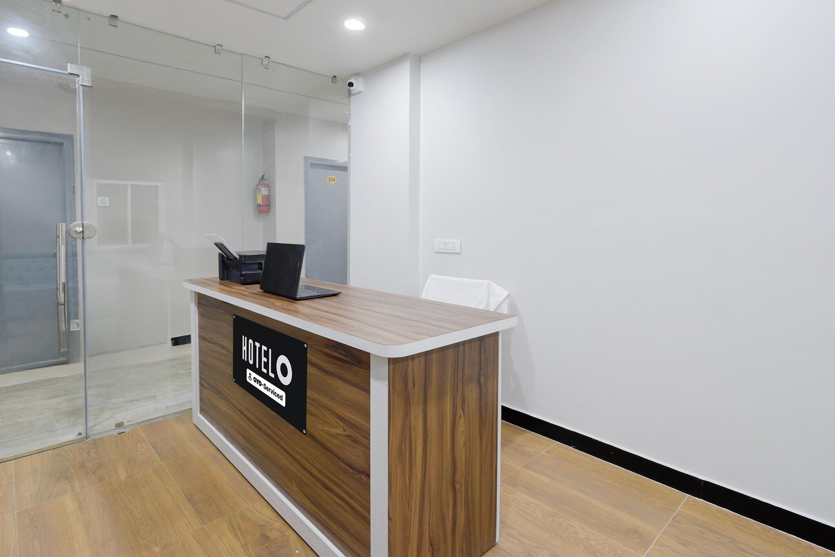 A hotel reception desk with a sign, a laptop, and a fire extinguisher on the wall.