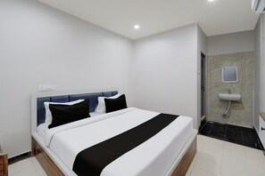 Ein Hotelzimmer mit Bett, Nachttisch, an der Wand montiertem Fernseher und einem Badezimmer mit Waschbecken und Spiegel.