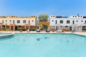 A swimming pool with lounge chairs and a covered seating area, surrounded by buildings with a modern architectural style. - La Villita de Panchi | Near Poblado, Pool & Tennis (Cabo Rojo)