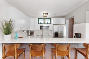 A modern kitchen with white cabinets, stainless steel appliances, and a bar area with wooden chairs. - La Villita de Panchi | Near Poblado, Pool & Tennis (Cabo Rojo)
