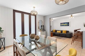 A modern living room with a glass dining table, sofas, and a large window. - La Villita de Panchi | Near Poblado, Pool & Tennis (Cabo Rojo)