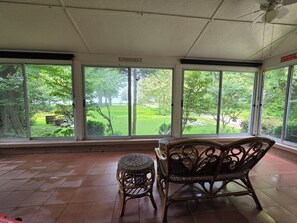 Ein Zimmer mit Blick auf einen Garten, durch großzügige Fenster, ein Korbstuhl und ein kleiner Hocker.