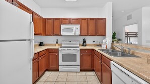 Eine moderne Küche mit Holzausstattung, einem weißen Kühlschrank, einer Mikrowelle, einem Backofen und einer Spüle.