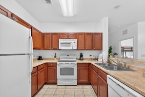 A modern kitchen with wooden cabinets, a white refrigerator, a microwave, an oven, and a sink. - Family & Pet Friendly Escape Near Disney (Kissimmee)