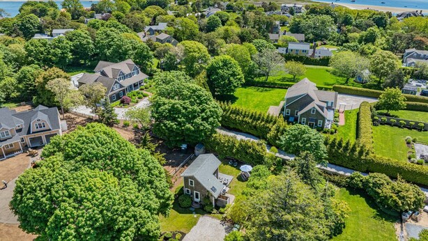 Luchtbeeld van een woongebied met huizen, groene gazons en een strand op de achtergrond.