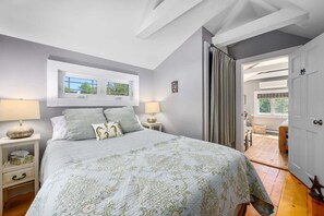 Ein Schlafzimmer mit einem Bett, zwei Nachttischen, einem Fenster und einer Tür, die auf einen Balkon führt.