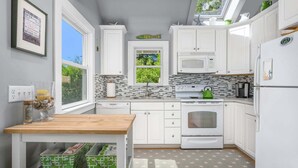 Een moderne keuken met witte kastjes, een magnetron, een oven en een groene waterkoker. Er is een raam met uitzicht op groen.