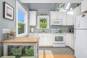 Eine moderne Küche mit weißen Schränken, einer Mikrowelle, einem Backofen und einem grünen Wasserkocher. Ein Fenster bietet Blick auf grüne Vegetation.