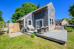 Ein zweistöckiges Haus mit einer Terrasse, einer Veranda und einem umzäunten Garten.