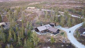 Eine abgelegene Holzhütte mit einer großen Terrasse, umgeben von dichtem Wald und einer unbefestigten Straße.