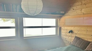 Ein Schlafzimmer mit einem Bett, zwei Fenstern, einer Pendelleuchte und einem Bücherregal.