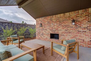 An outdoor patio with a brick wall, a fireplace, and wooden furniture. - The Foundry - 5BR/3.5BA - Family Retreat (Lubbock)