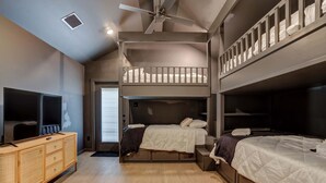 Una habitació amb llits superposats, televisió, una petita commode de fusta i ventilador al sostre.
