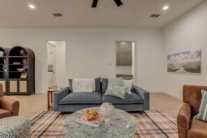 A living room with a sofa, armchairs, a coffee table, and a bookshelf. - The Foundry - 5BR/3.5BA - Family Retreat (Lubbock)