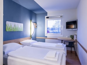 A hotel room with two beds, a TV, a window with a view, and a painting on the wall. - Ibis Budget Bremen City Sud (Bremen)