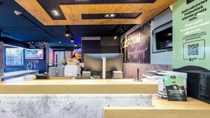 En modern hotellobby med ett träpanelat tak, en digital skärm som visar information och en receptionsdisk med en kaffemaskin och en skylt som erbjuder gratis frukost.