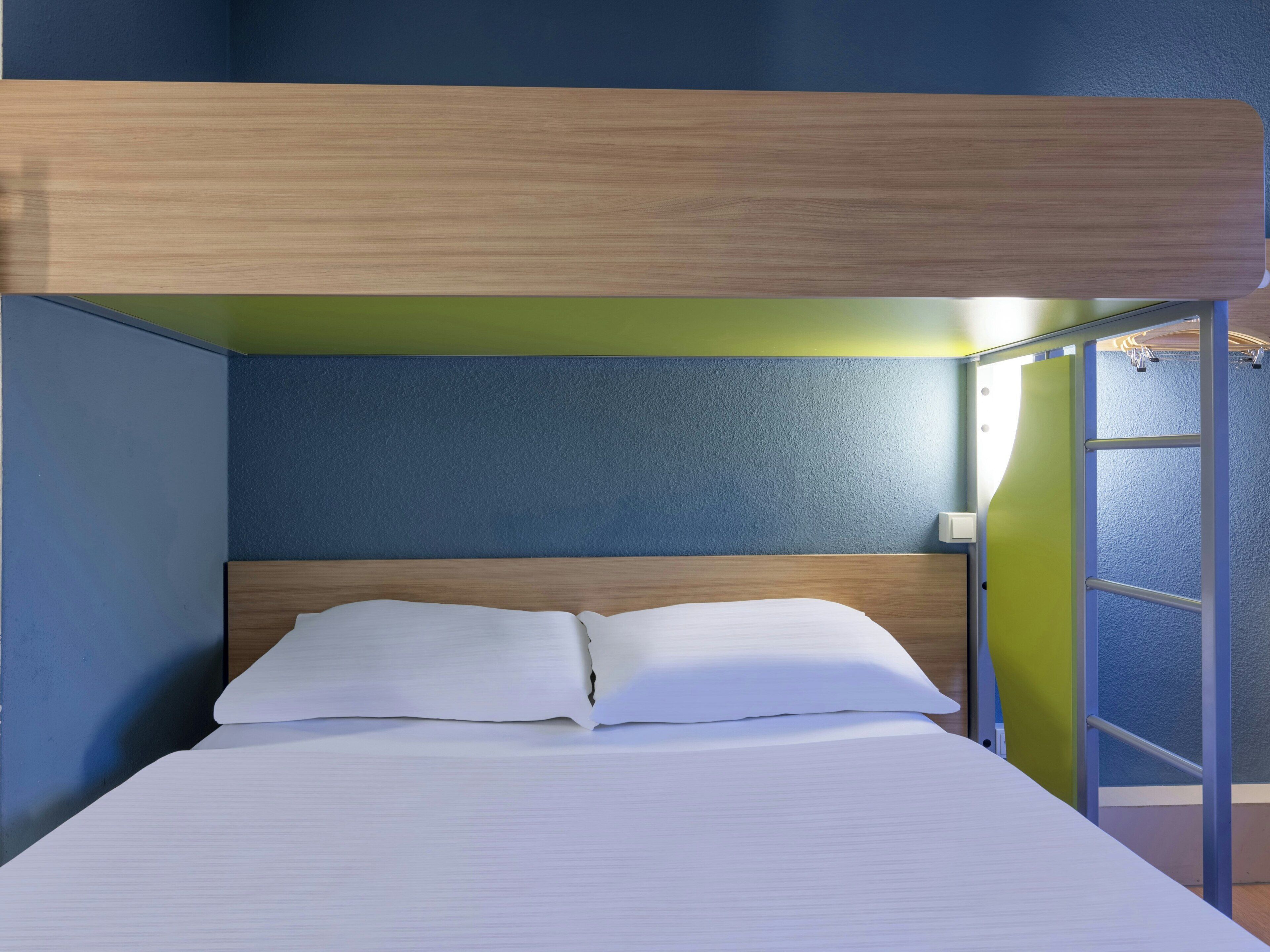 A bunk bed with a wooden headboard, white bedding, and a green accent wall.