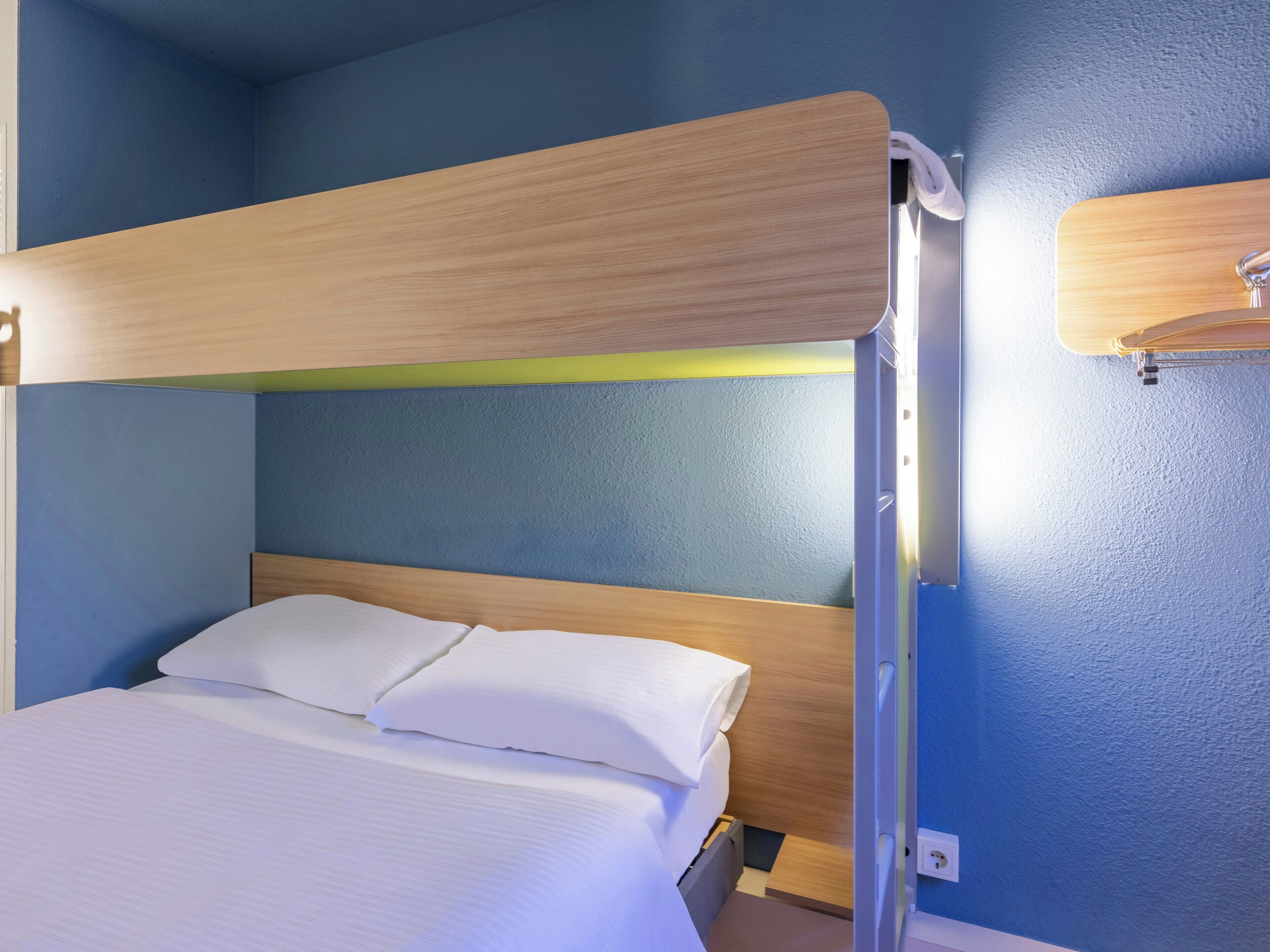 Una cama individual con cabecera de madera, ropa de cama blanca y pared azul.