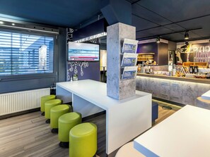 A modern hotel reception area with a large digital screen, a counter with a menu, and green bar stools. - B B Hotel Bremen Sud (Bremen)