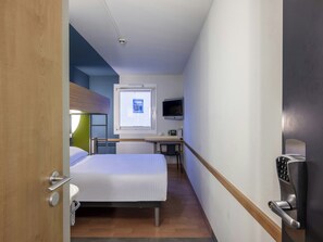 Habitació d'hotel amb llit, escriptori, televisió i finestra.