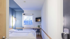 Ett hotellrum med två sängar, ett skrivbord, en tv och ett fönster med utsikt över träd.