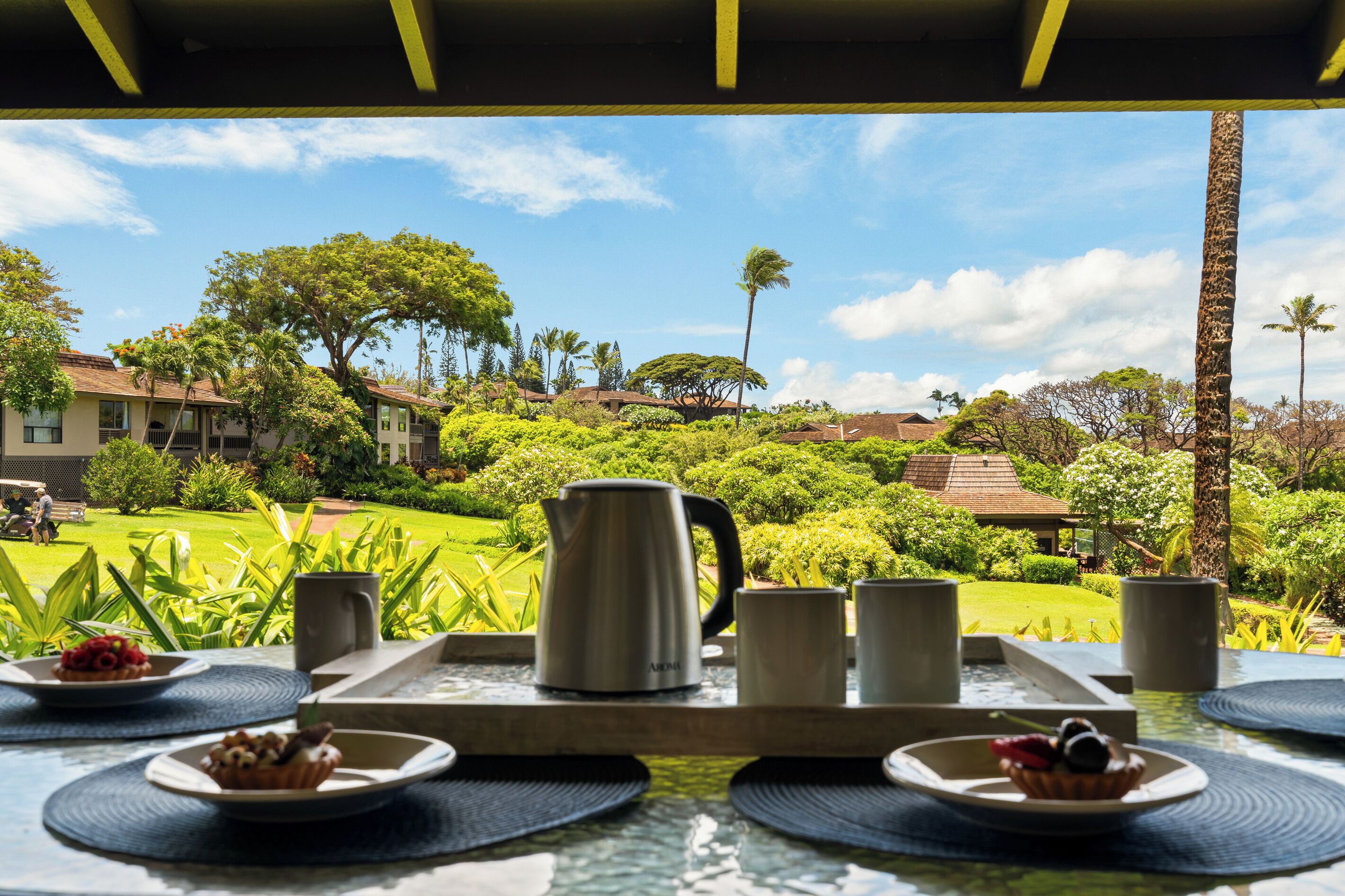 A breakfast table with a view of a lush garden and buildings.