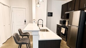 Una cocina moderna con encimera blanca, armarios oscuros y electrodomésticos de acero inoxidable.