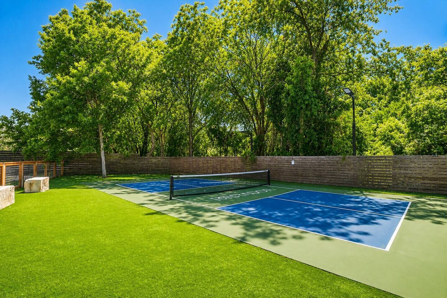 Ein Tennisplatz im Freien mit Netz, umgeben von einer Ziegelmauer und Bäumen.