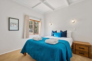 A bedroom with a bed, a window with curtains, a bedside table, and a wall-mounted light fixture. - Lime Tree Cottage - Mt Roskill (Mt Roskill)