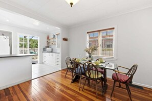 A modern kitchen with wooden flooring, white cabinetry, and a dining area with a table set for four. - Lime Tree Cottage - Mt Roskill (Mt Roskill)