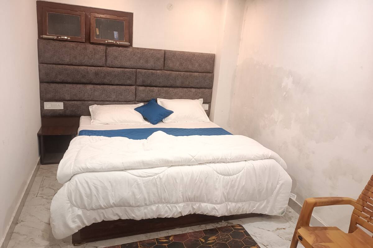 A bedroom with a bed, a headboard, a nightstand, a chair, and a wall-mounted TV.