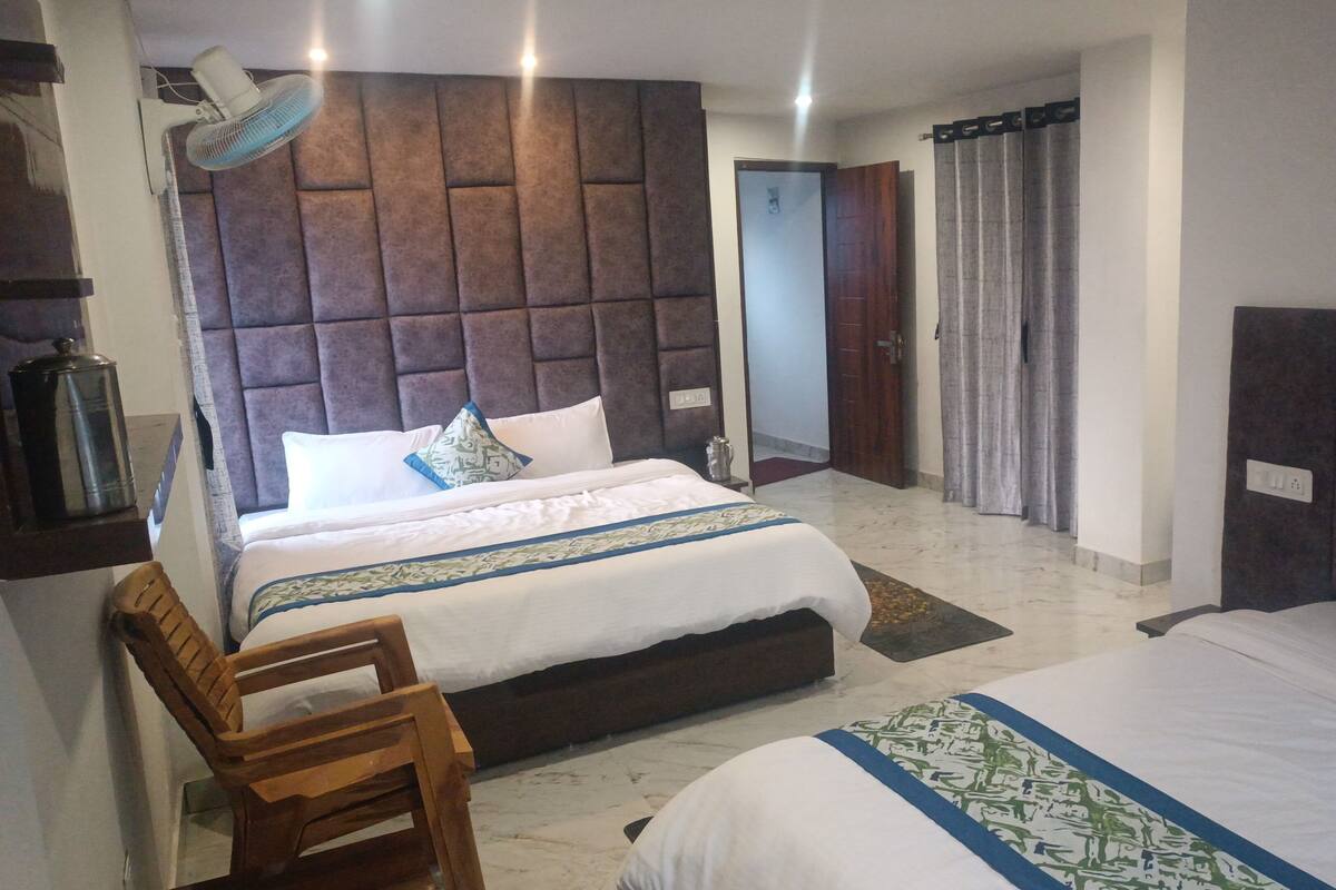 A hotel room with two beds, a wooden chair, a fan, and a large padded headboard.